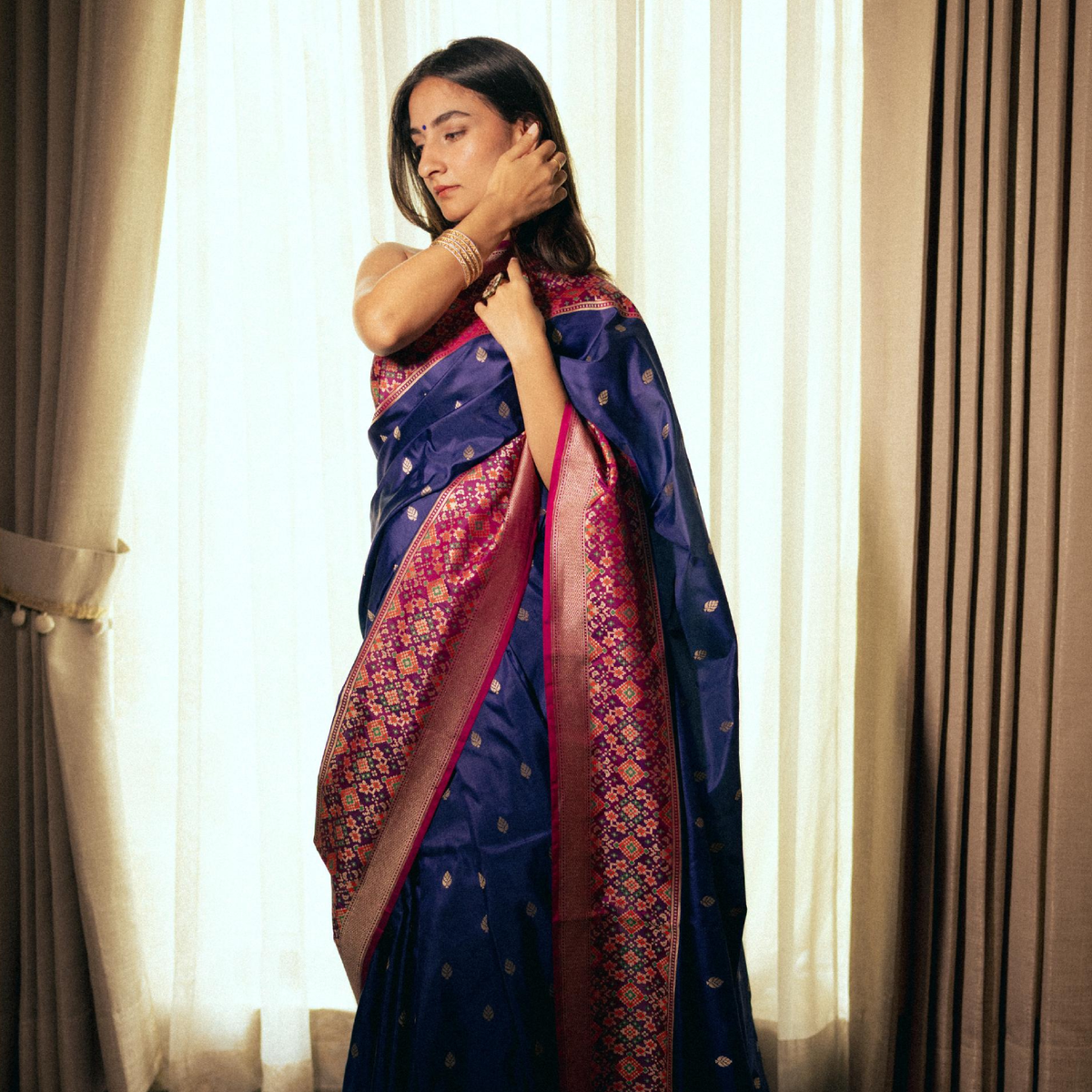 A model wearing an elegant dark blue silk saree with a decorative pink border and intricate gold patterns, draped traditionally