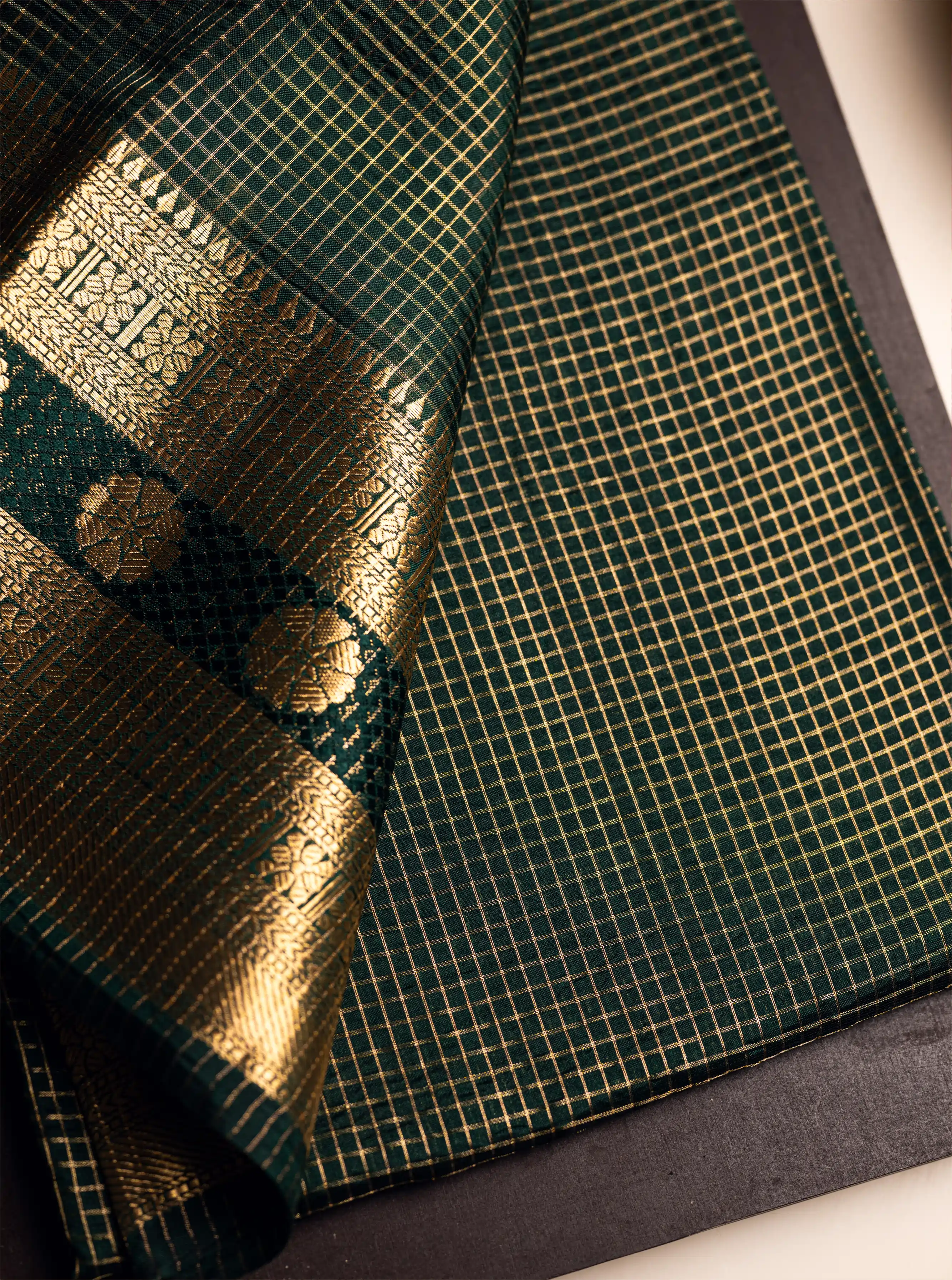 Close-up of the green Handwoven Pure Katan Silk Saree showing the gold zari check pattern and traditional floral border on a dark background.