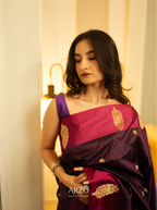 Woman wearing a purple saree with gold embroidery in a softly lit room.