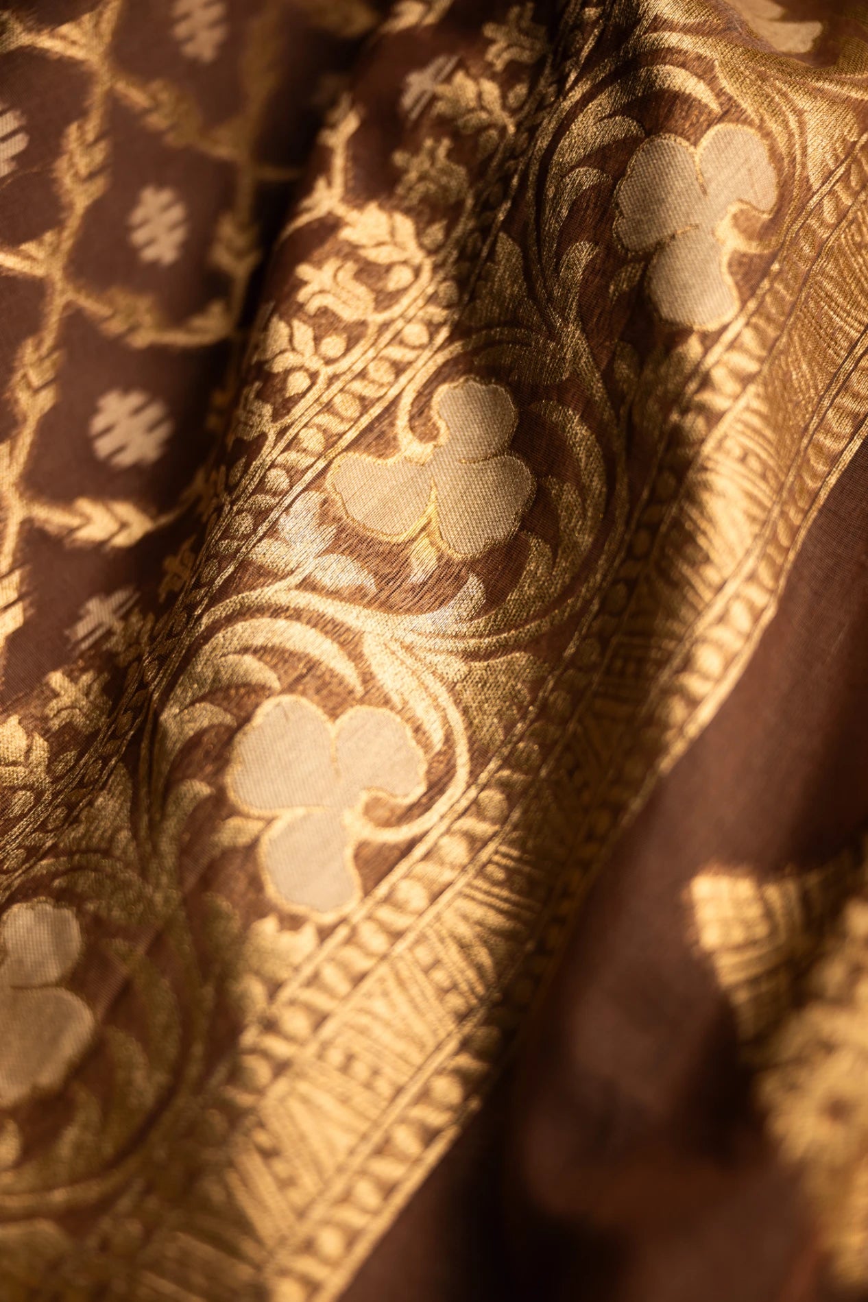 Close-up of the intricate gold zari floral embroidery on a brown Jamdani silk cotton saree, showing the delicate hand-loomed craftsmanship and fabric texture.