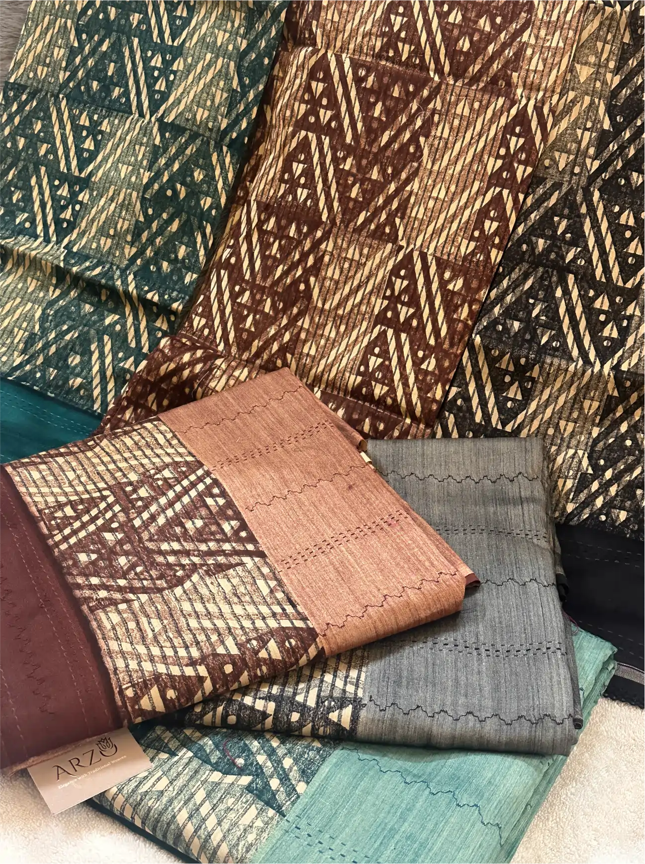 Close-up view of folded cotton fabrics with intricate geometric patterns and a branded Arzo tag.