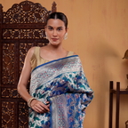 Model draped in a blue Azure Meenakari Majesty Katan Silk Saree with handwoven Shikargah patterns and a gold border, posing against a wooden backdrop.