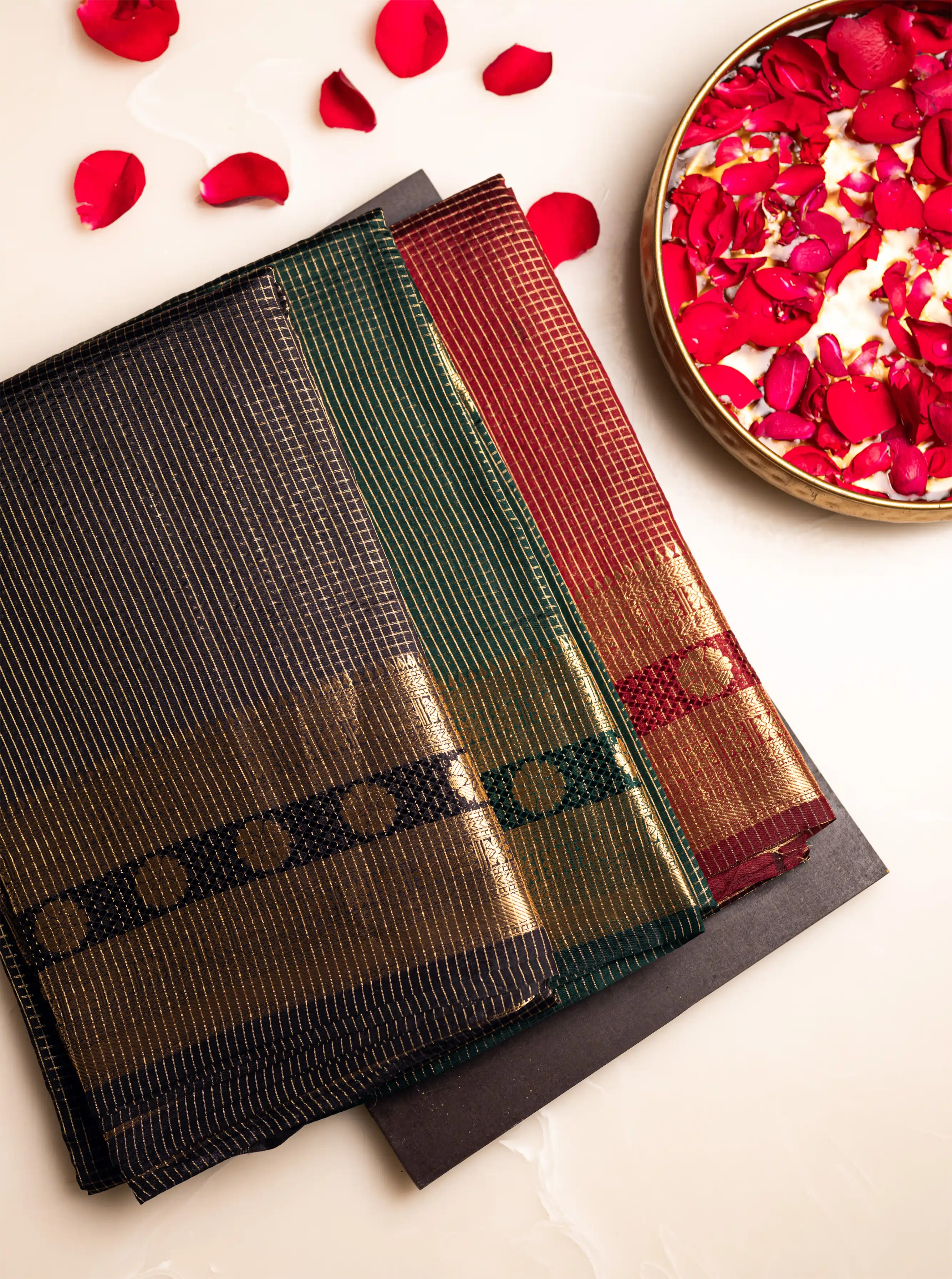 Elegant black Handwoven Pure Katan Silk Saree with a gold zari border and traditional check pattern, styled with red rose petals on a white background.
