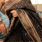 Close-up detail of a premium black handwoven Katan silk saree showcasing a metallic gold zari diamond check pattern and a structured geometric border.