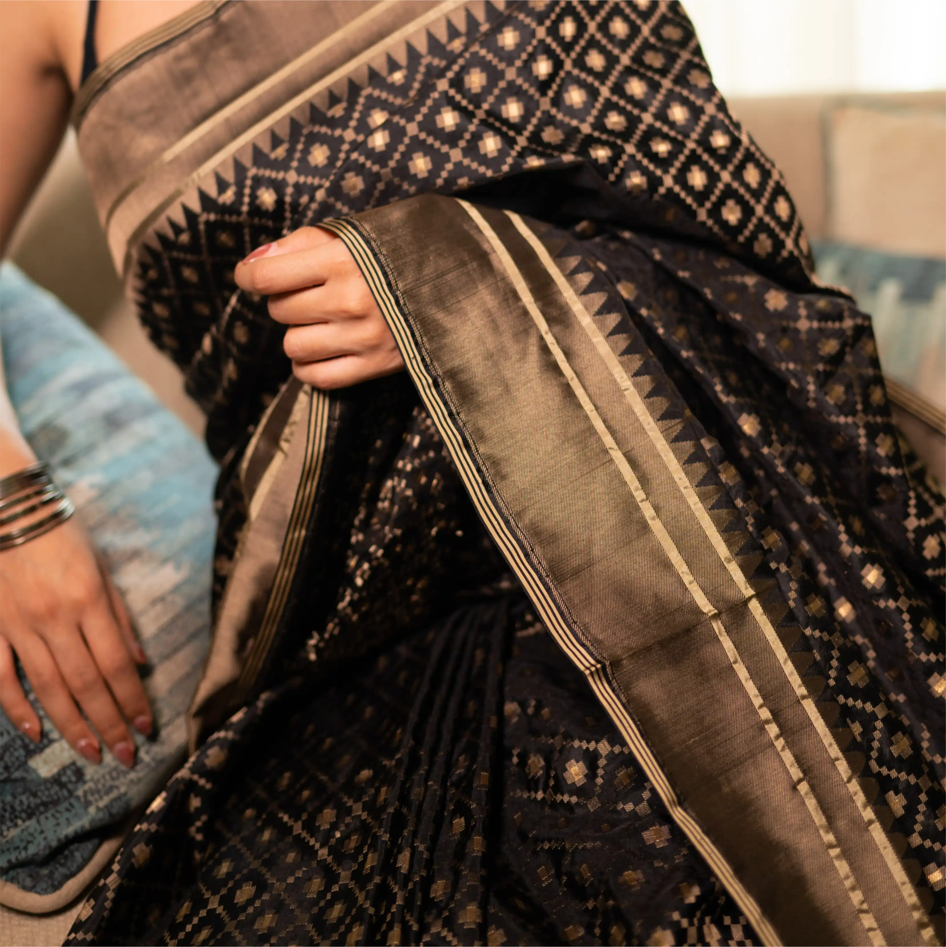 Close-up detail of a premium black handwoven Katan silk saree showcasing a metallic gold zari diamond check pattern and a structured geometric border.