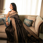 Lifestyle shot of a model in a Black Handwoven Katan Silk Saree, showcasing the intricate gold zari weave and luxurious drape in a seated pose.