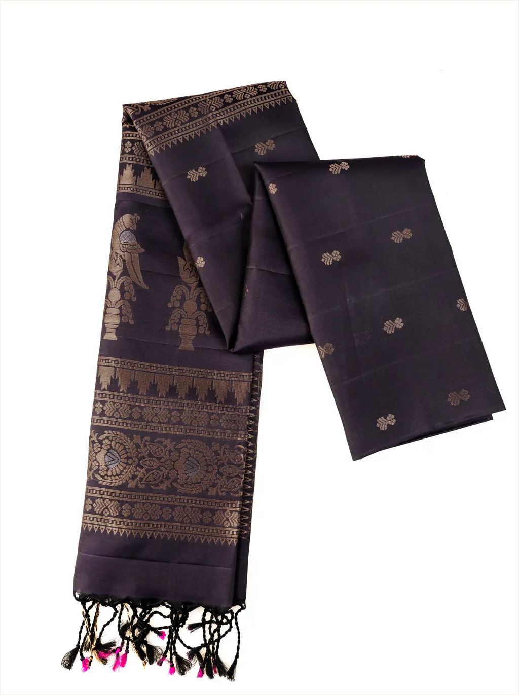 Deep black pure Patola silk saree folded against a plain white backdrop, highlighting fine gold zari motifs scattered across the body, a wide traditional zari-woven border, and black and bright pink knotted tassels along the fringe of the pallu.