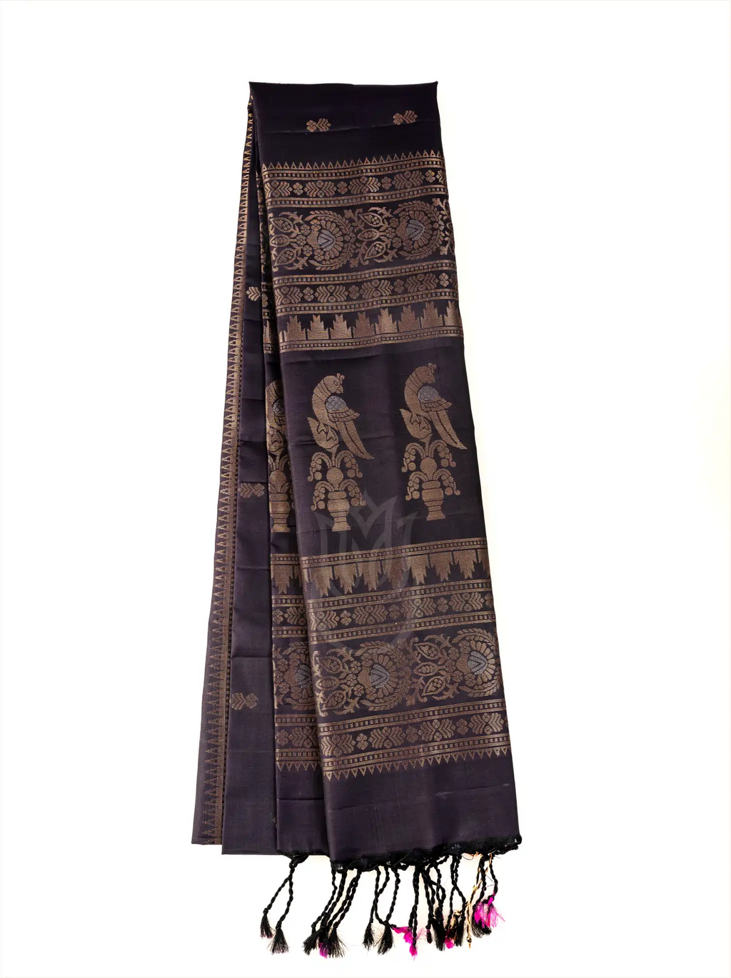 Deep black pure Patola silk saree displayed lengthwise on a white background, highlighting two large gold zari peacock motifs on the top layer, intricate geometric zari band weaving across the body, and black tassels with vibrant pink tied accents along the bottom fringe.