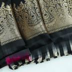 Close-up of a premium black silk blouse fabric featuring intricate traditional gold zari weaving patterns and a soft, lustrous texture.