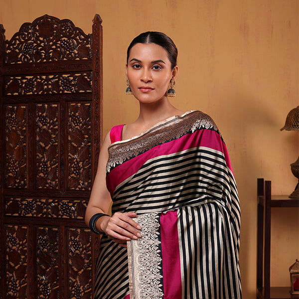 A woman showcasing a sophisticated black and white striped saree, featuring a vibrant fuchsia pink border and pallu, perfect for festive and traditional occasions.