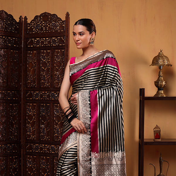 A woman wearing an elegant black and white striped saree with a striking fuchsia pink border and pallu, styled for festive and traditional occasions.