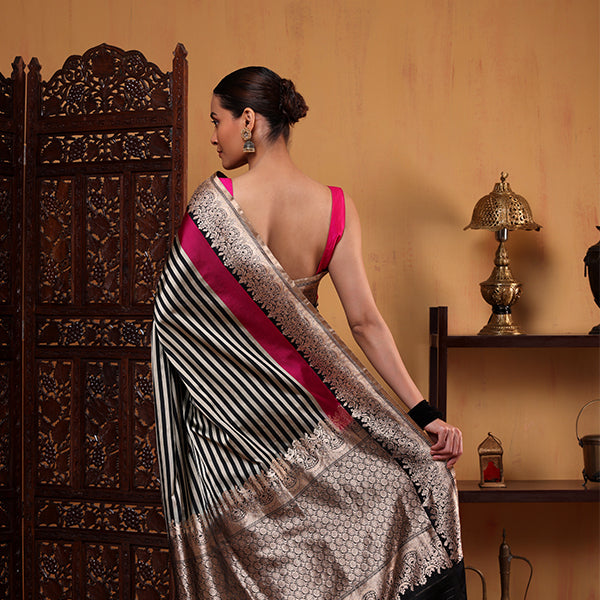 A woman wearing an elegant black and white striped saree featuring a vibrant fuchsia pink border and pallu, styled for a traditional festive occasion.
