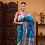 Model wearing a handwoven Blue Azure Shikargah Katan Silk Saree with a gold Meenakari border, paired with a vibrant pink sleeveless blouse.