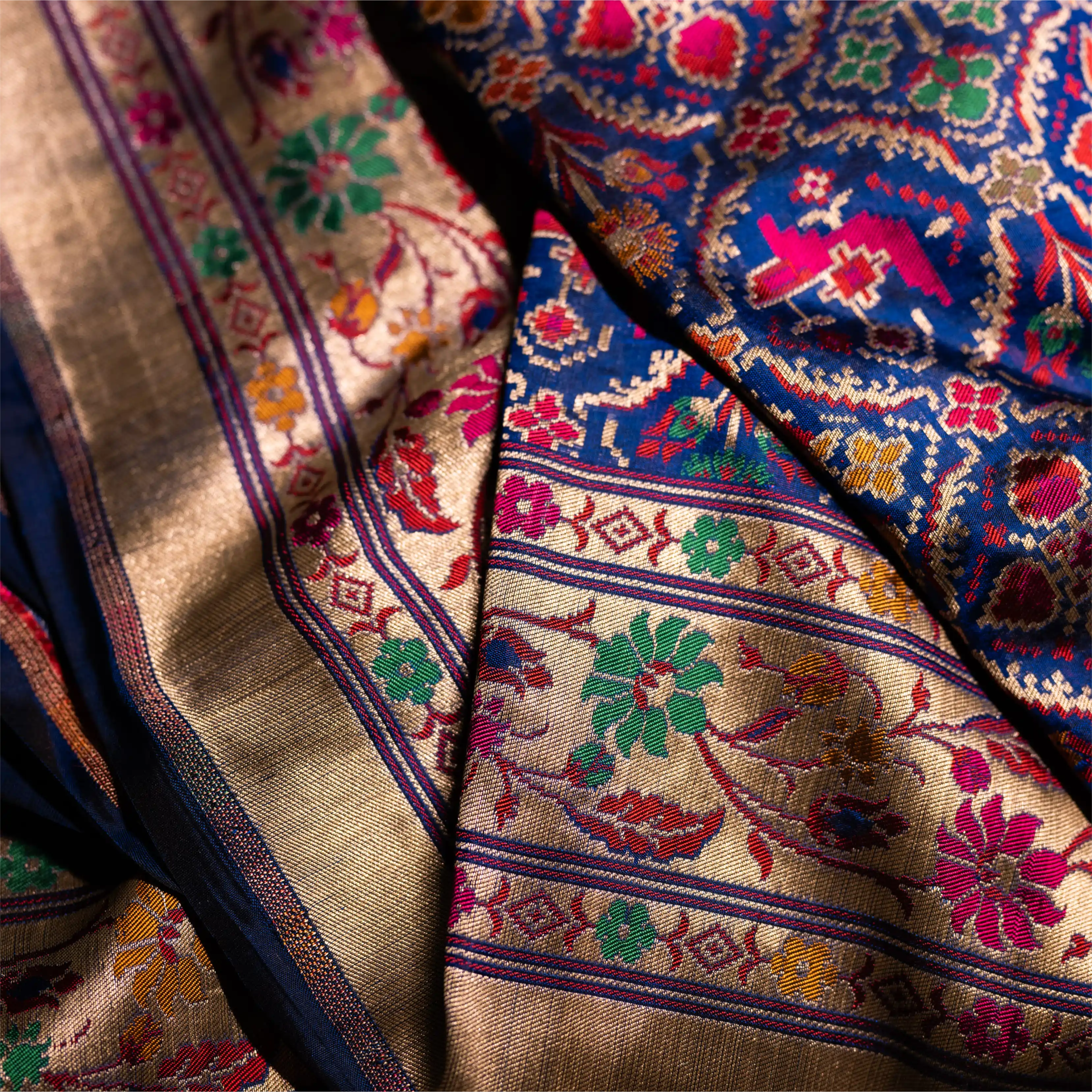 Close-up drape of a royal blue Paithani Patola silk saree showing the contrast between the geometric ikat patterns and the floral zari border.