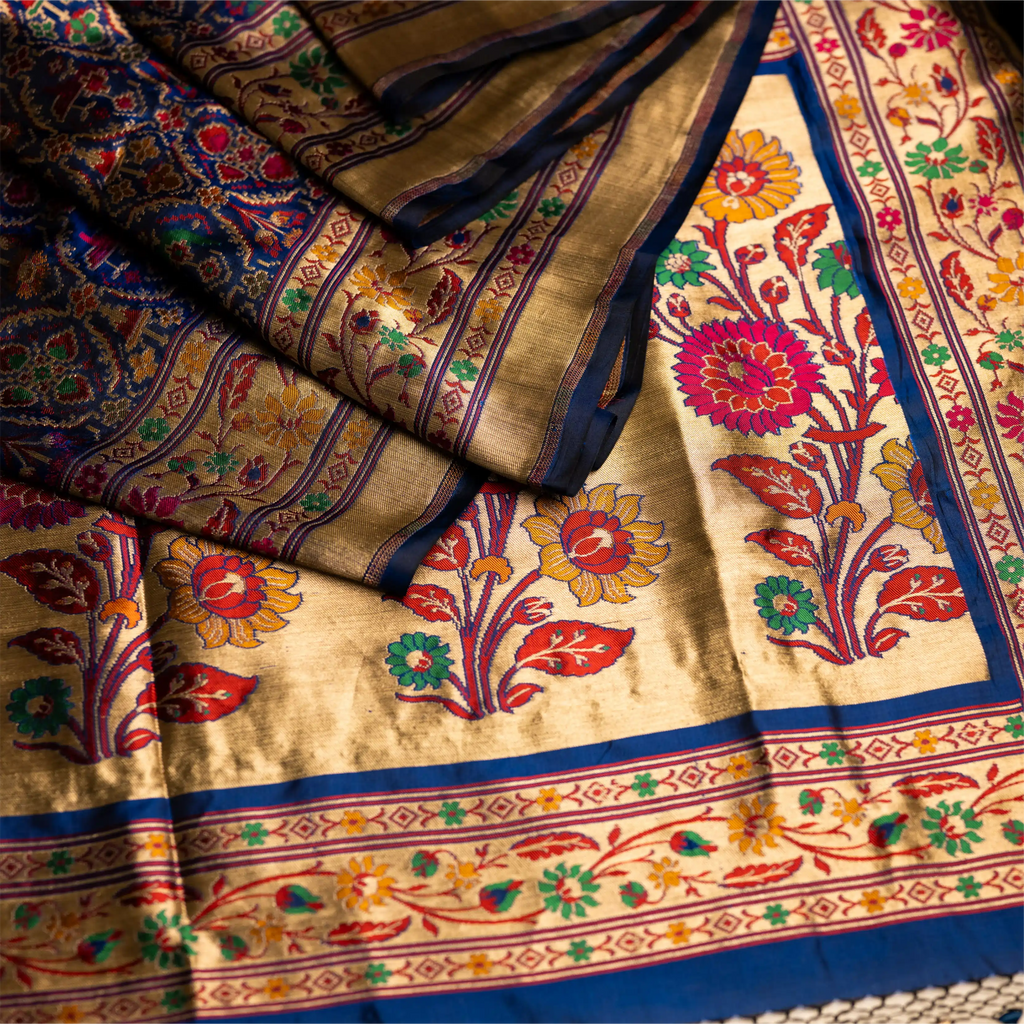 Close-up of the royal blue Paithani Patola silk saree pallu featuring handwoven colorful parrot motifs and an intricate gold zari floral border.