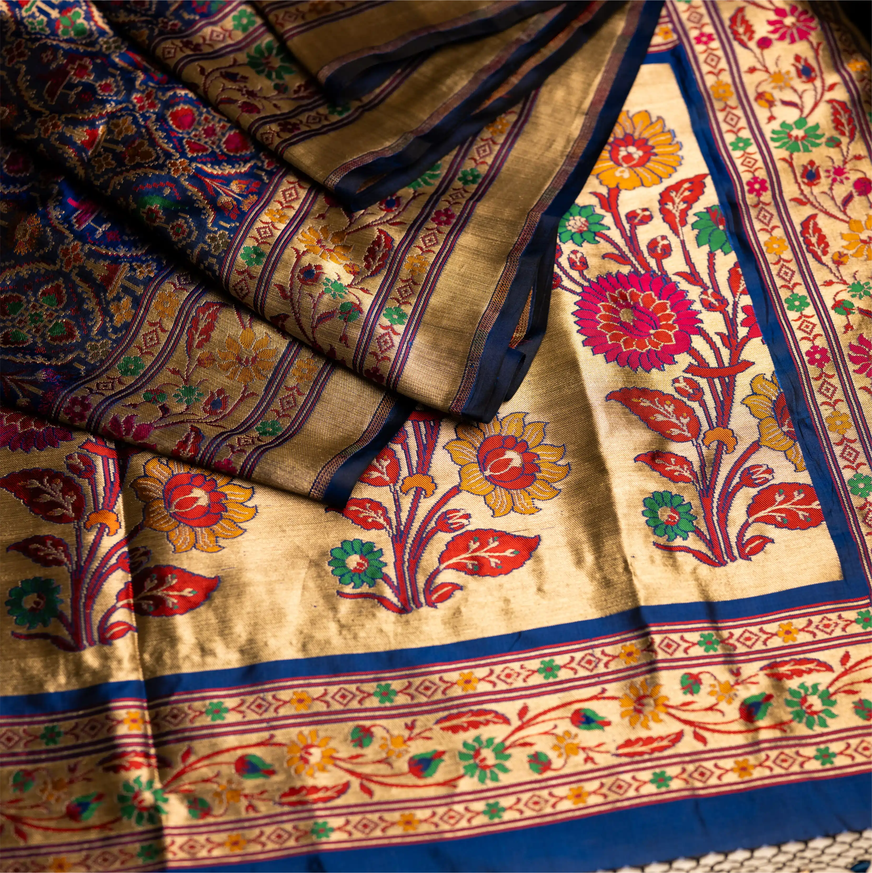 Close-up of the royal blue Paithani Patola silk saree pallu featuring handwoven colorful parrot motifs and an intricate gold zari floral border.
