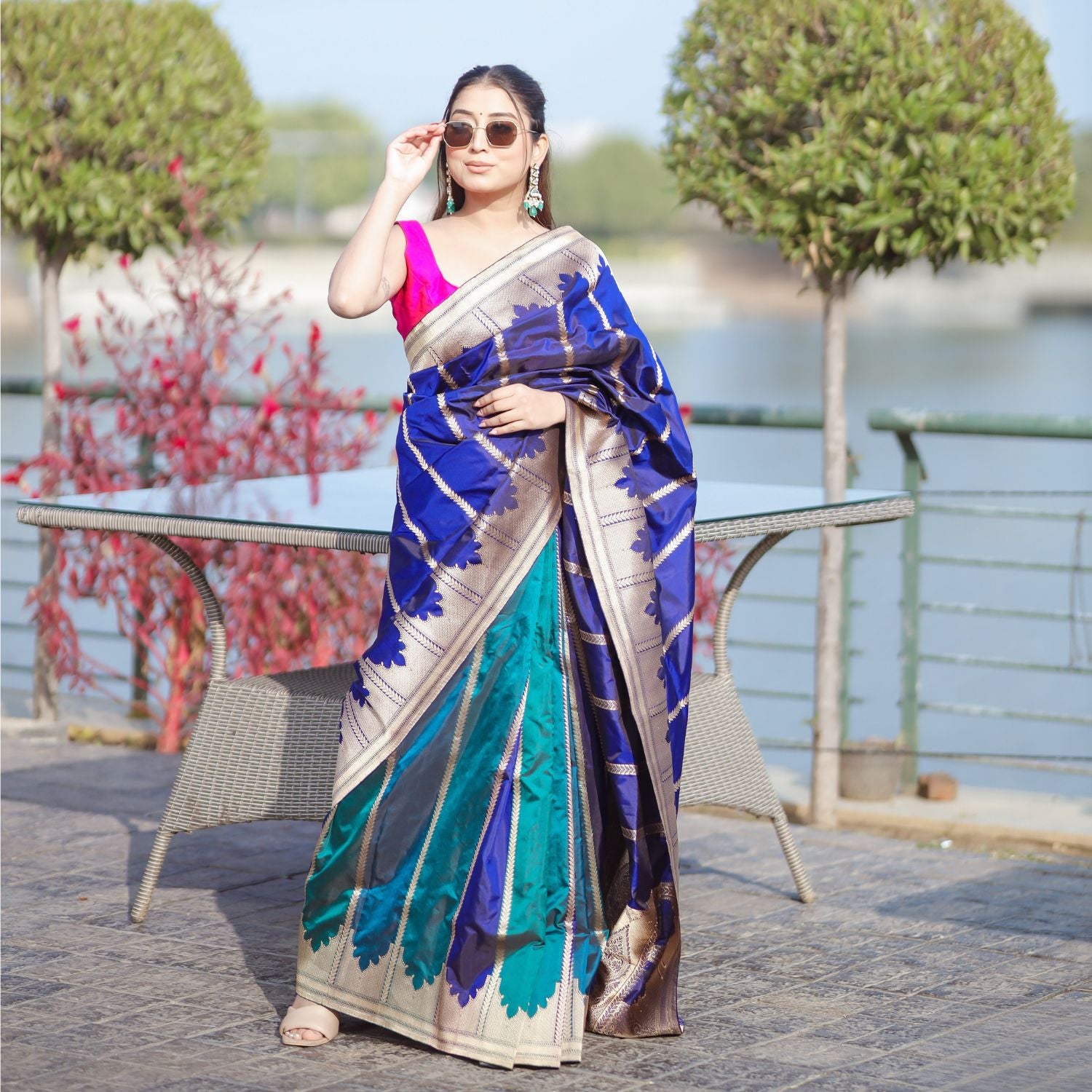 A model wearing a premium blue and teal Patola silk saree with a traditional woven design, paired with a vibrant pink sleeveless blouse.