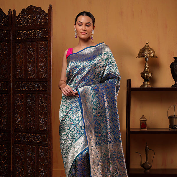 Model wearing the Blush Shikargah Elegance Katan Silk Saree showcasing its intricate gold zari jaal weaving and teal blue base, beautifully styled with a vibrant pink sleeveless blouse.