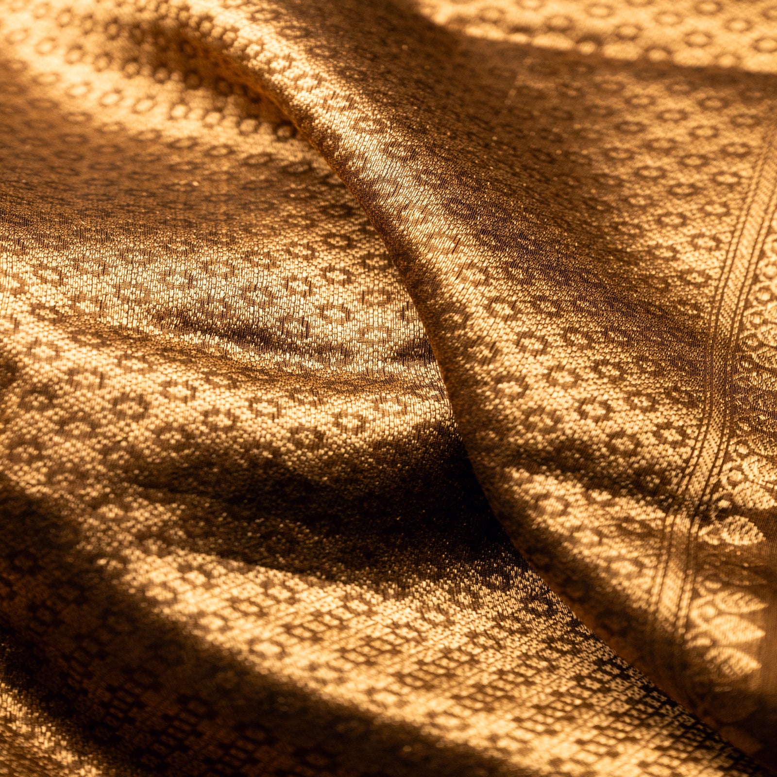 Extreme close-up of the intricate gold zari weaving on an earthy brown Alfi silk saree, showcasing the traditional hand-loomed texture and pattern.