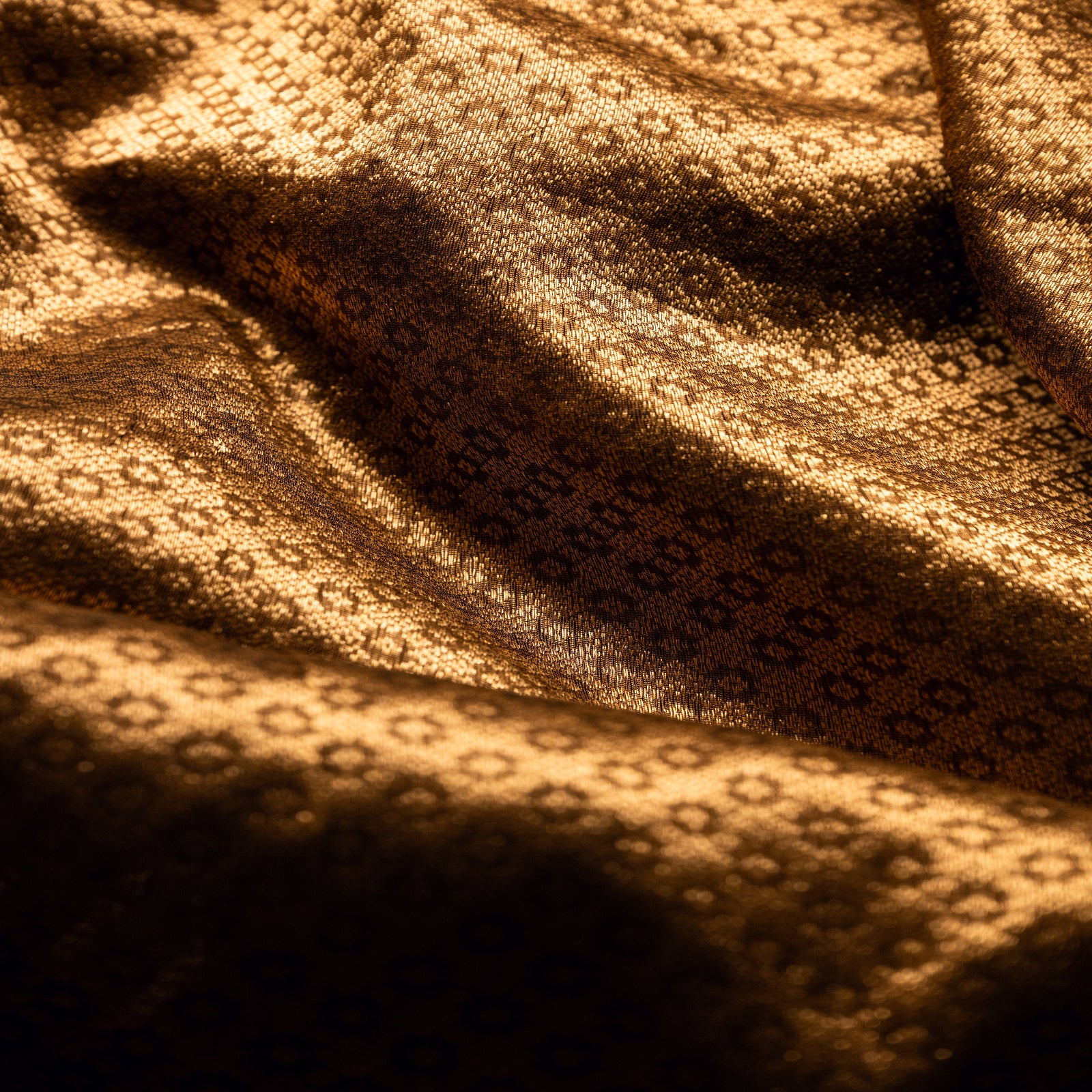 High-angle view of the soft folds of a brown Alfi silk saree, showcasing the consistent pattern of gold zari buta and the fabric's luxurious sheen.
