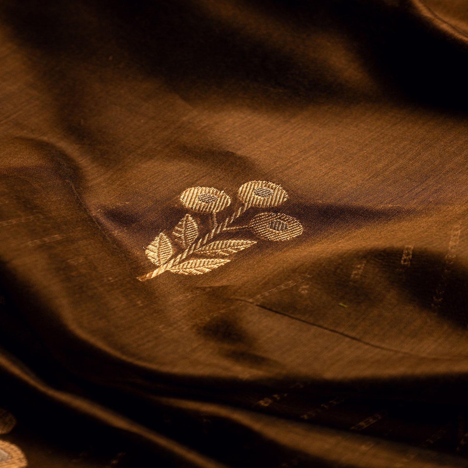 Detailed close-up of a hand-loomed gold zari floral motif on earthy brown Alfi silk fabric.