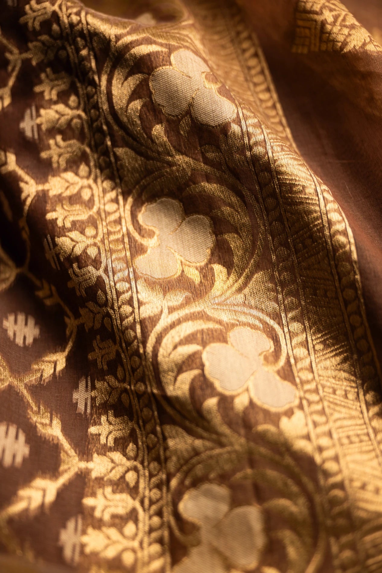 Wide view of an earthy brown Jamdani silk cotton saree showing the elegant drape and the detailed gold zari border work.