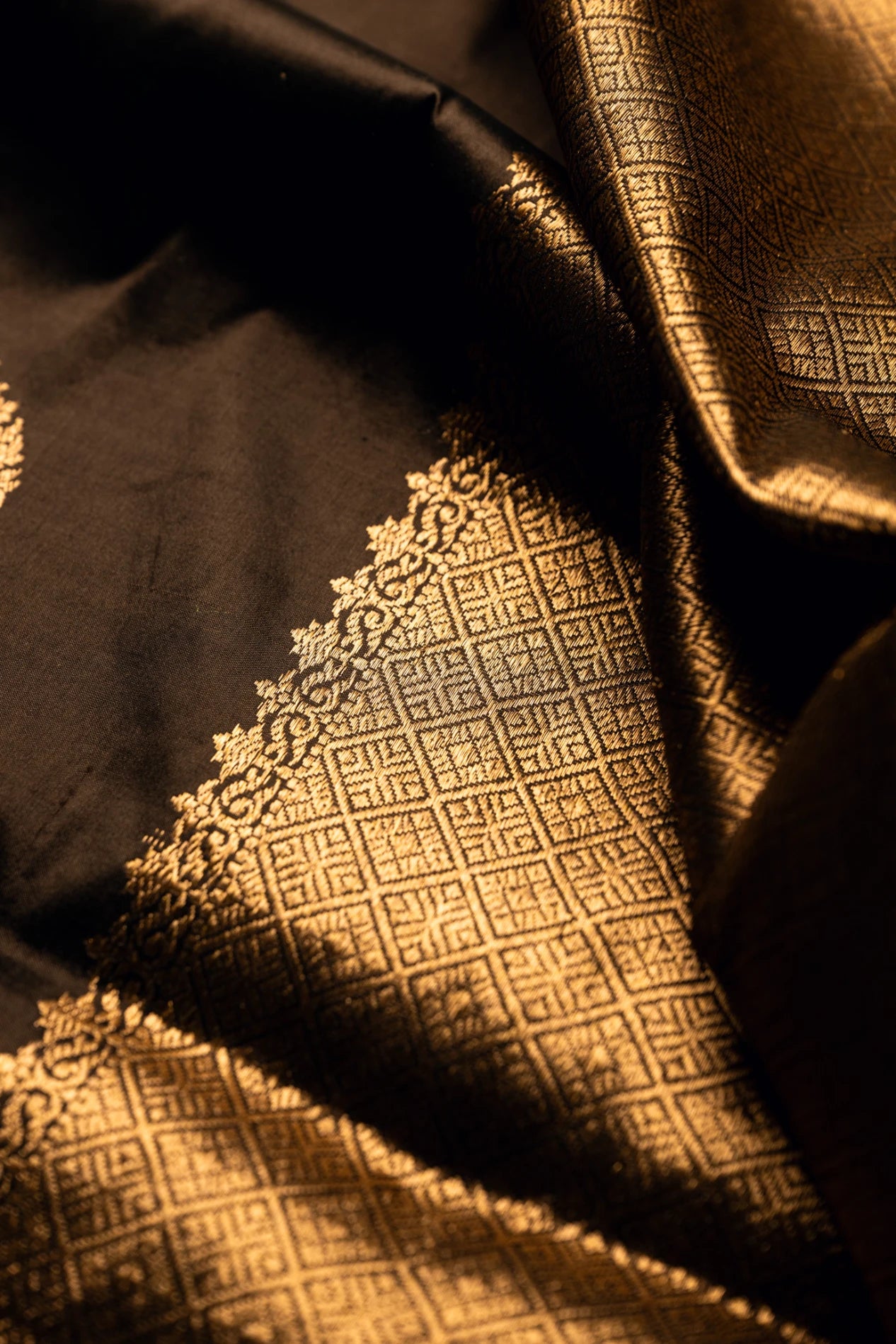 Close-up detail of an earthy brown Jamdani silk cotton saree showcasing an ornate handwoven gold zari floral border and geometric grid pattern textures.