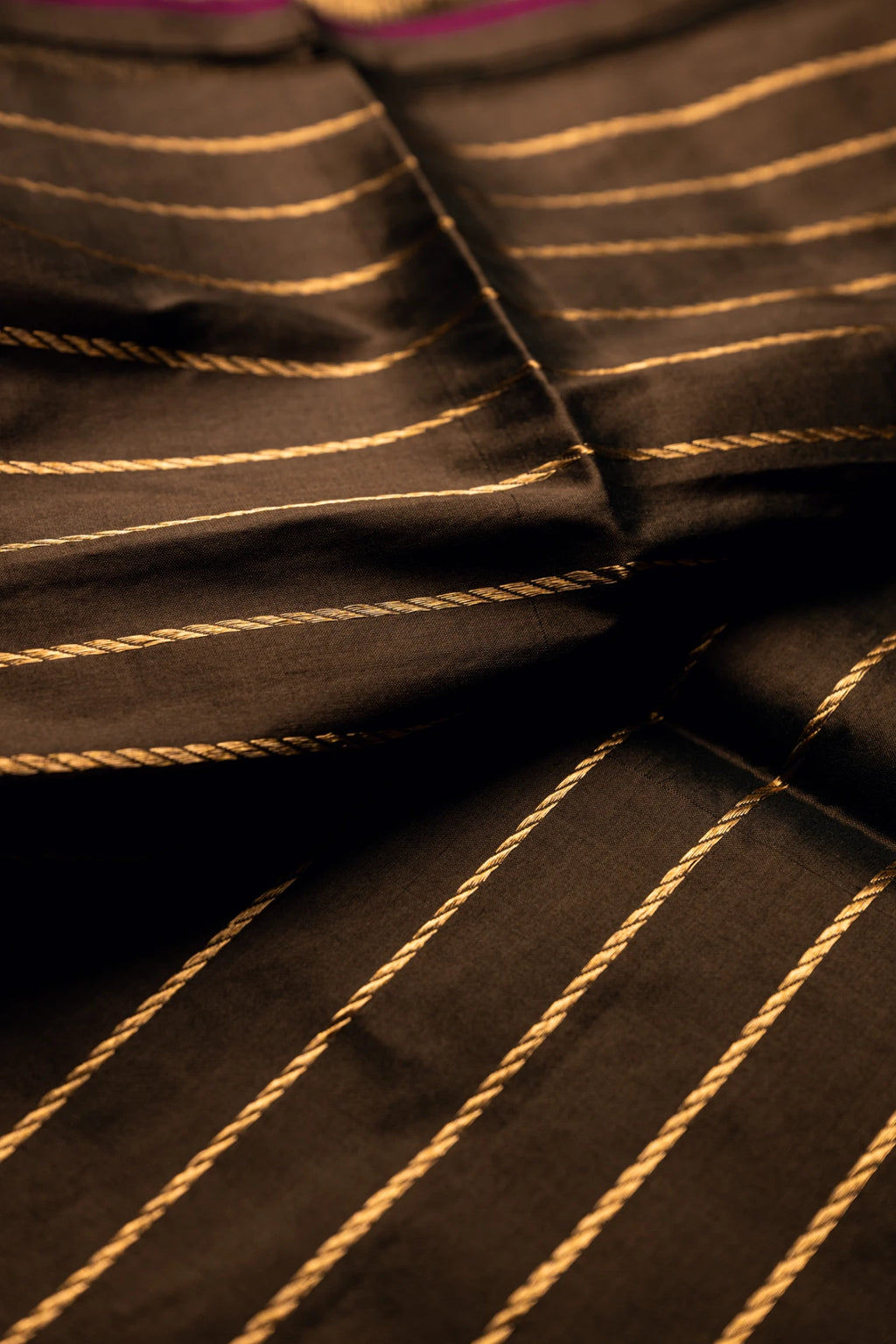 Close-up of the crisp pleated folds of an earthy brown Jamdani silk cotton saree showcasing elegant handwoven diagonal gold zari stripes.