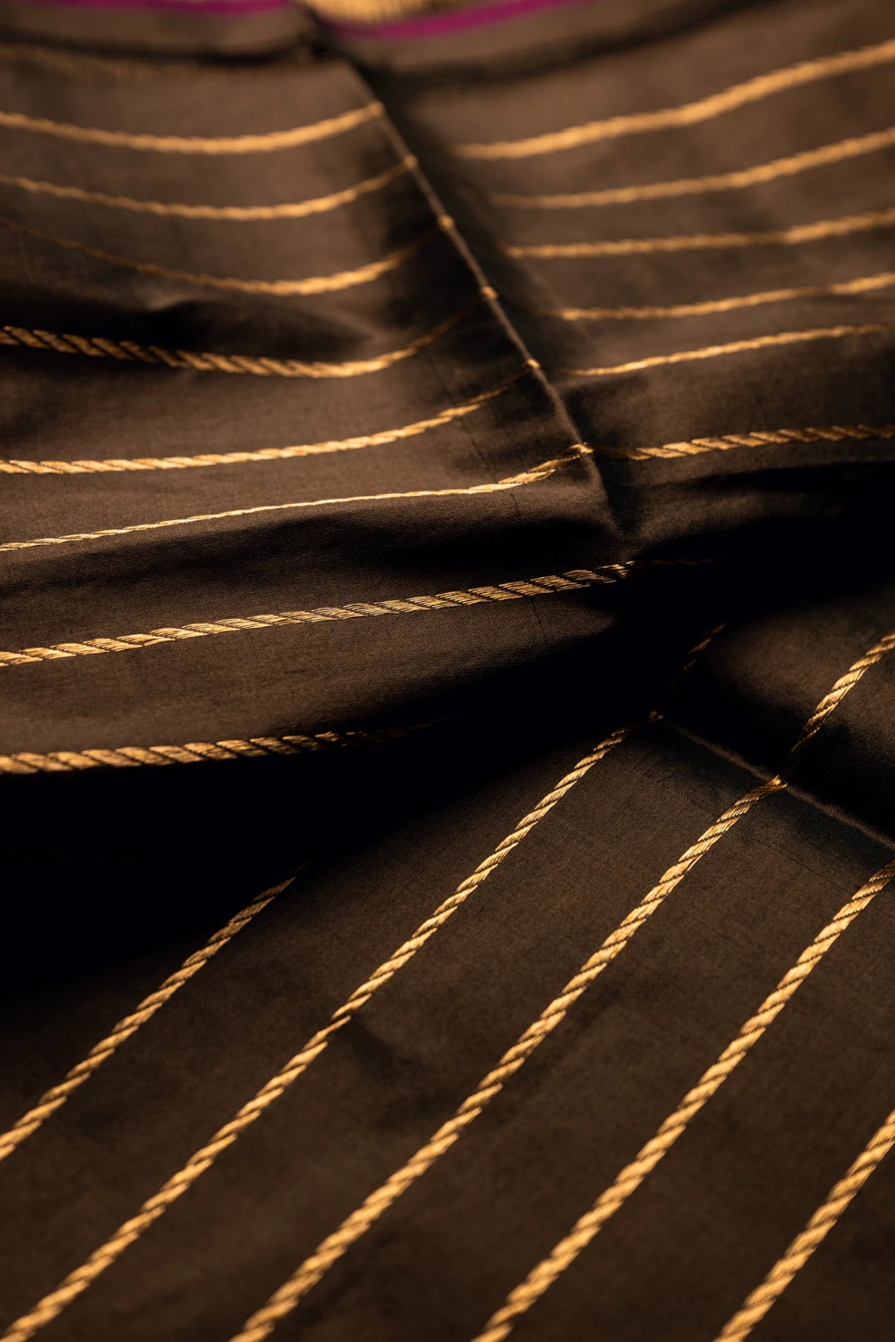 Close-up of the crisp pleated folds of an earthy brown Jamdani silk cotton saree showcasing elegant handwoven diagonal gold zari stripes.