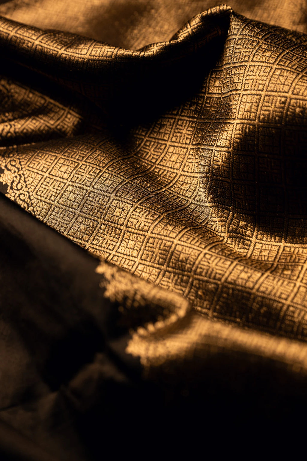 Close-up of the rich, textured folds of an earthy brown Jamdani silk cotton saree highlighting the shimmering handwoven gold zari geometric grid patterns.