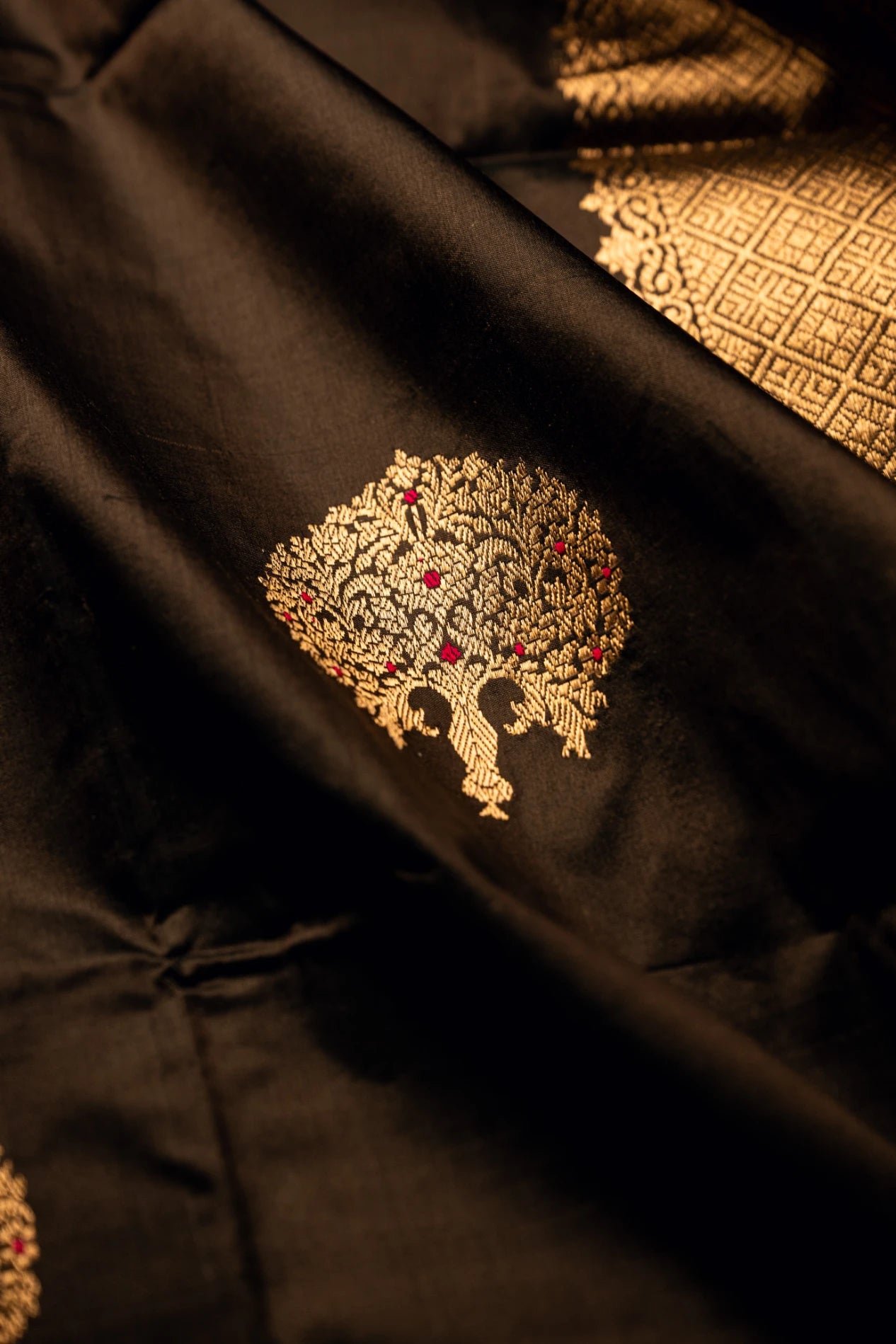 Close-up detail of an earthy brown Jamdani silk cotton saree showcasing a traditional handwoven gold zari tree motif and rich textured fabric folds.