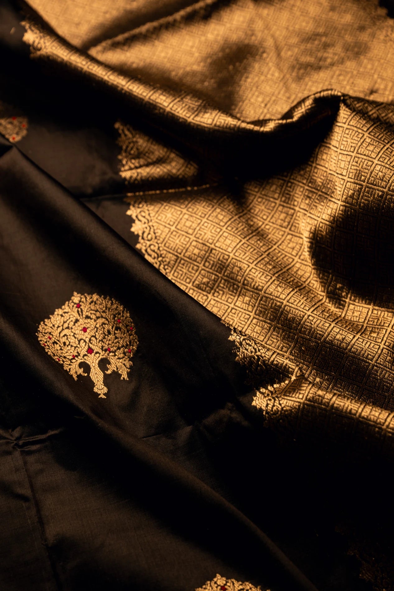 Close-up of the rich textured folds of an earthy brown Jamdani silk cotton saree highlighting handwoven gold zari geometric grid patterns and a decorative woven tree motif.