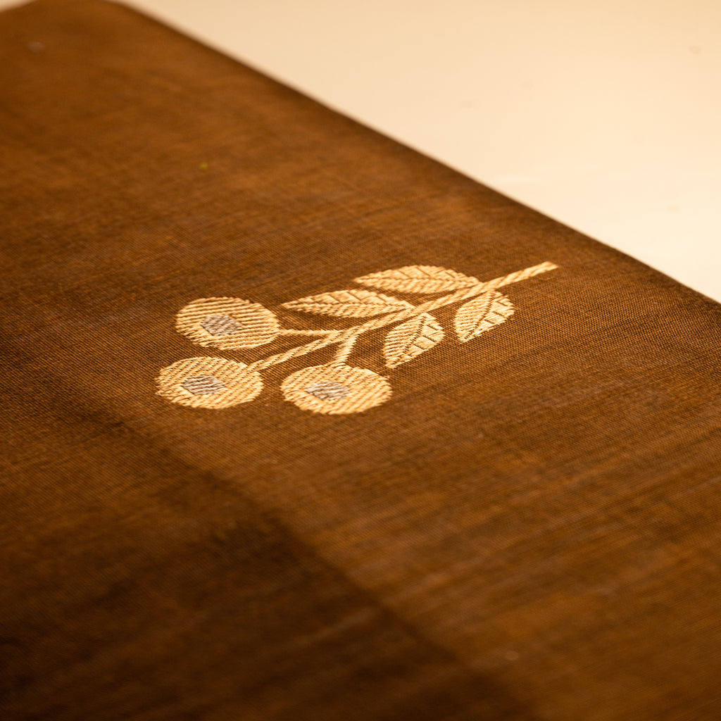 Close-up of a single hand-loomed gold zari floral and leaf motif on a brown Alfi silk saree, highlighting the precise threadwork.
