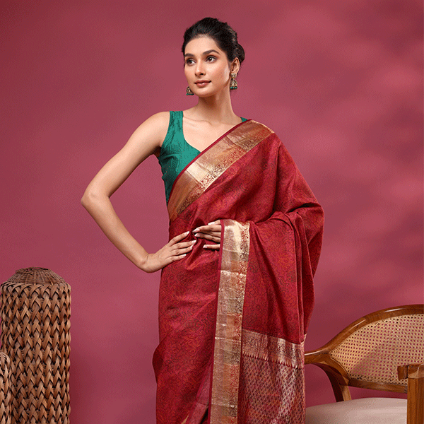 Model wearing the Crimson Celestial Dawn Silk Saree featuring an elegant handwoven zari pallu and border, beautifully paired with a solid teal green sleeveless blouse.