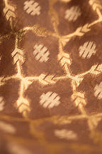Close-up detail of a brown Jamdani silk cotton saree showing the hand-loomed gold zari floral motifs and textured fabric weave.