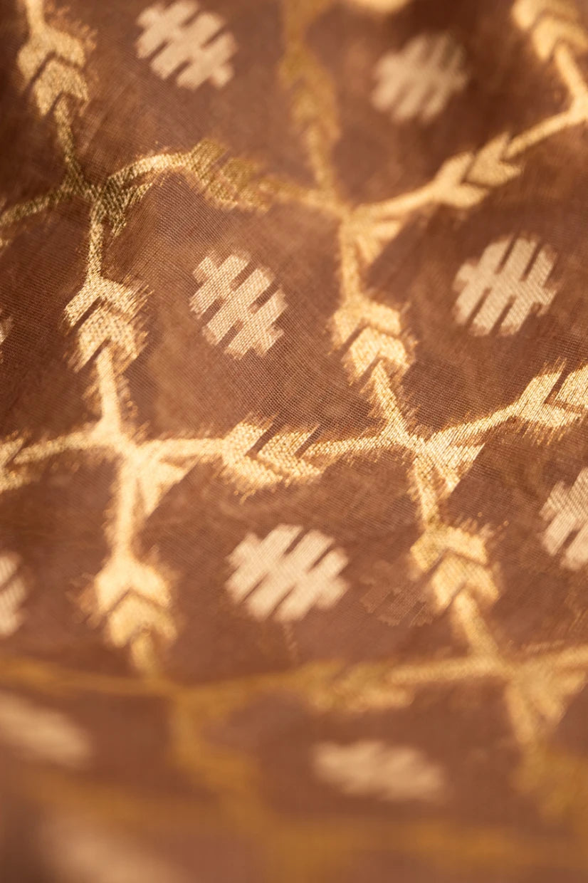 Close-up detail of a brown Jamdani silk cotton saree showing the hand-loomed gold zari floral motifs and textured fabric weave.