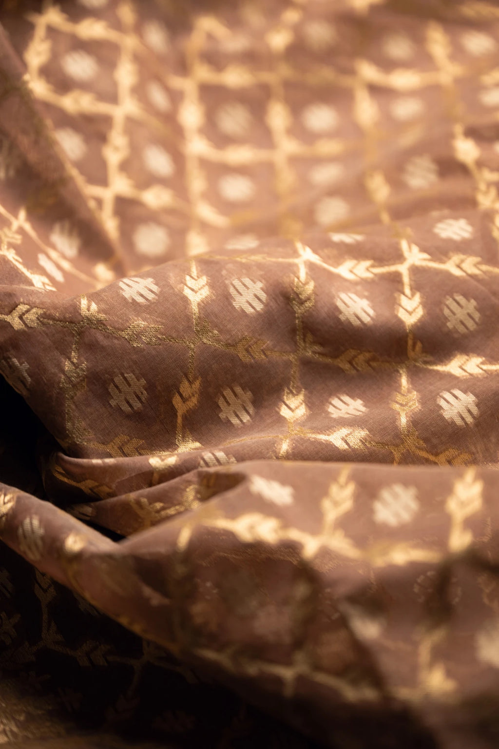 Close-up detail of a brown Jamdani silk cotton saree showing the hand-loomed gold zari floral motifs and textured fabric weave.