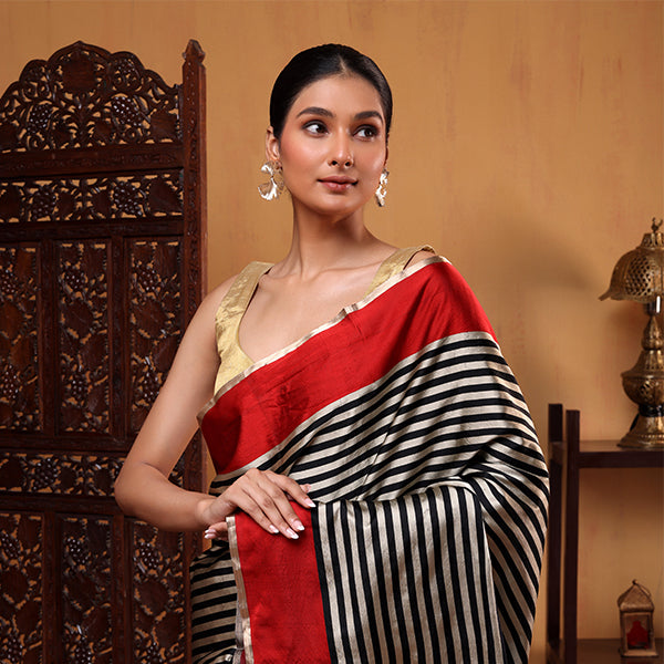 Model wearing the Crimson Majesty Satin Saree featuring a bold crimson red base, classic black and white stripes, paired with a gold zari blouse.