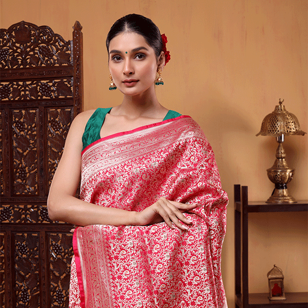 Model wearing the Crimson Shikargah Splendor Katan Silk Saree in rich red with an intricate gold zari jaal pattern and a green sleeveless blouse.