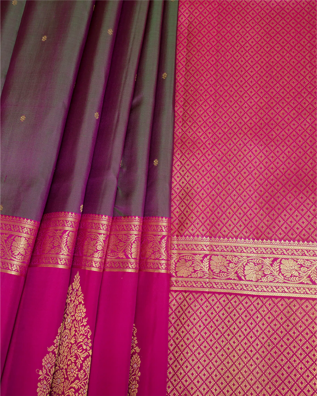 A close-up of a richly patterned silk saree, showing a dark plum purple body with small gold motifs, a bright magenta-pink border, and detailed gold zari brocade work