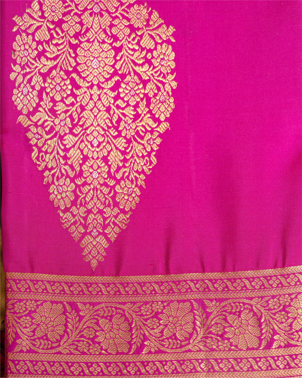 Close-up of a bright pink Kanjivaram silk saree featuring a large ornate gold brocade paisley motif and a detailed woven border along the bottom.