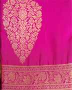 Close-up of a bright pink Kanjivaram silk saree featuring a large ornate gold brocade paisley motif and a detailed woven border along the bottom.