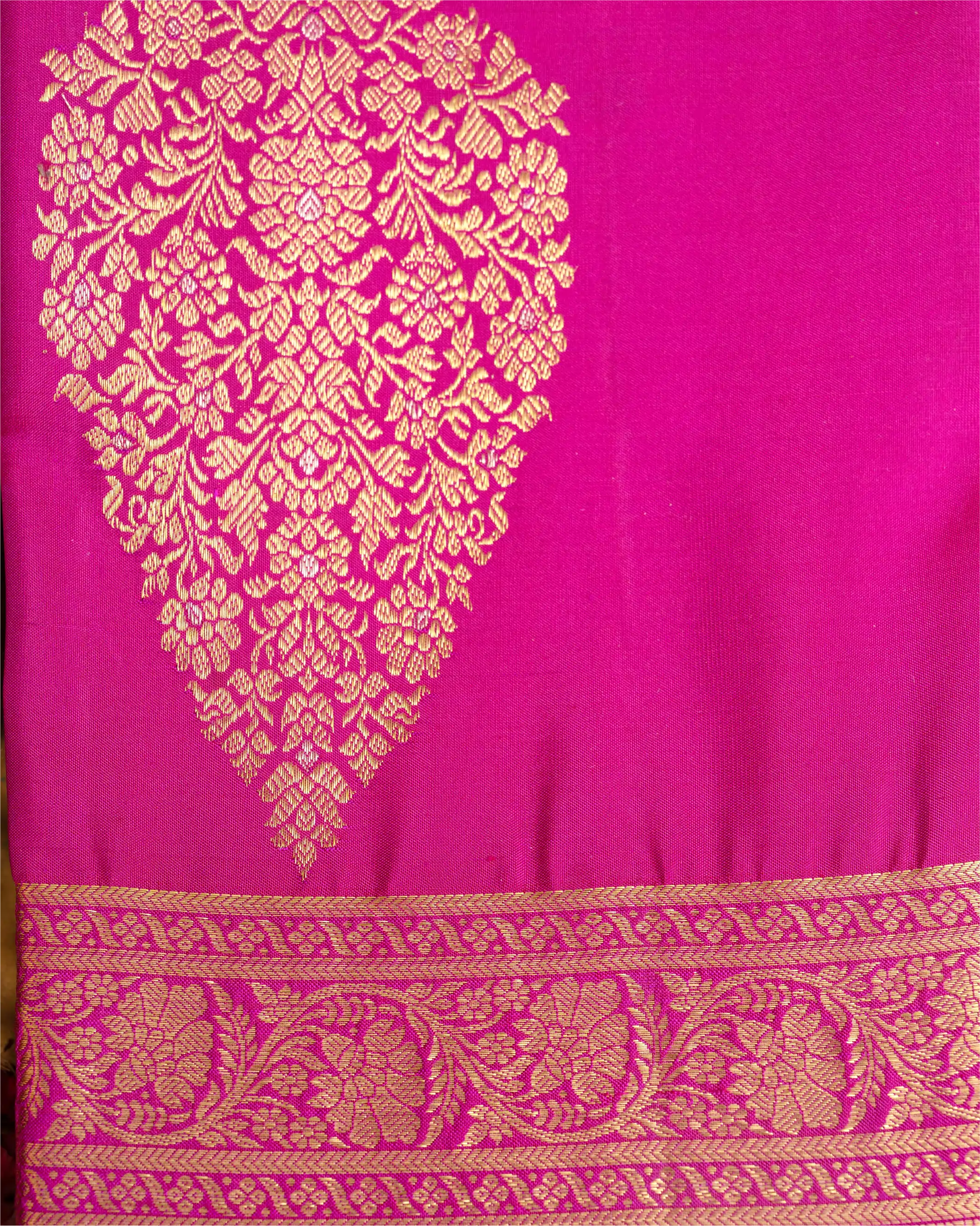 Close-up of a bright pink Kanjivaram silk saree featuring a large ornate gold brocade paisley motif and a detailed woven border along the bottom.