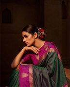 Close-up of a dark green and magenta Kanjivaram silk saree showcasing the detailed gold zari woven pallu and ornate floral motifs."