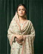 A woman wearing an elegant, light-colored Chanderi silk suit set featuring delicate floral patterns and intricate embroidery, perfect for festive occasions.
