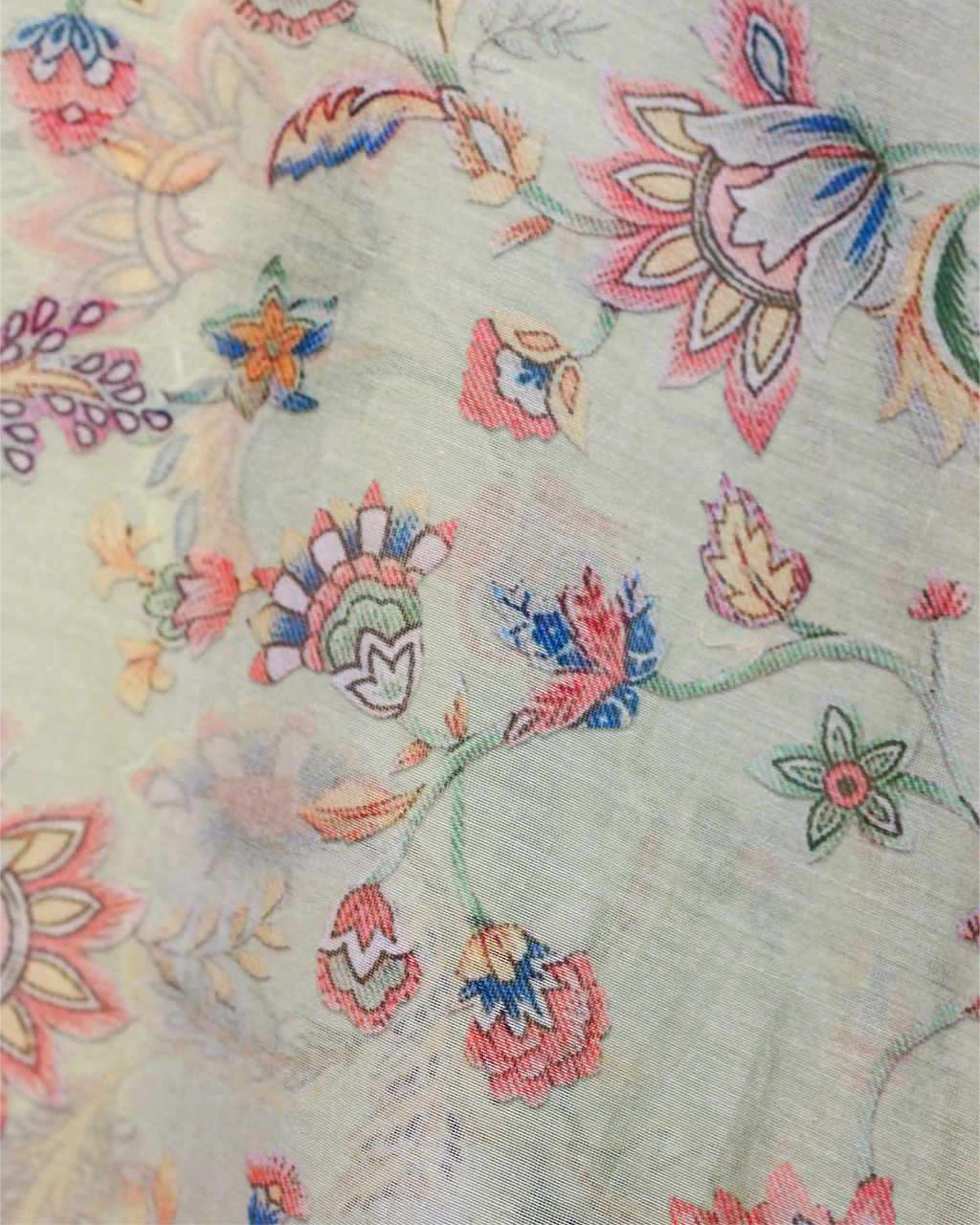 A detailed close-up of a light beige fabric featuring an intricate, multicolored floral and vine embroidery pattern, showcasing artisanal craftsmanship.
