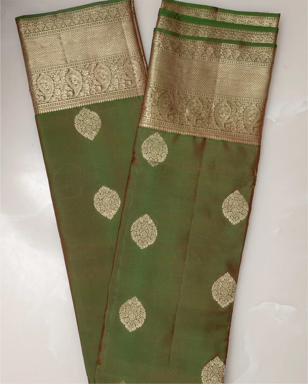 A neatly folded olive green Kanjivaram silk saree displayed on a traditional brass plate.