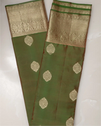 A neatly folded olive green Kanjivaram silk saree displayed on a traditional brass plate.