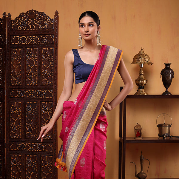 Woman posing in a premium fuchsia pink Tussar Georgette silk saree featuring an intricate multicolored weave border and elegant navy blue sleeveless blouse.