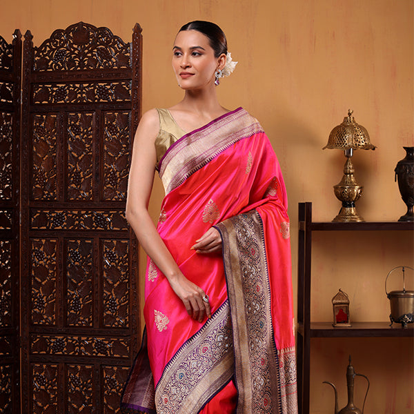 Woman wearing a vibrant fuchsia pink katan silk saree with handwoven gold sauna rupa boota work and a detailed traditional border, paired with a sleeveless golden blouse.